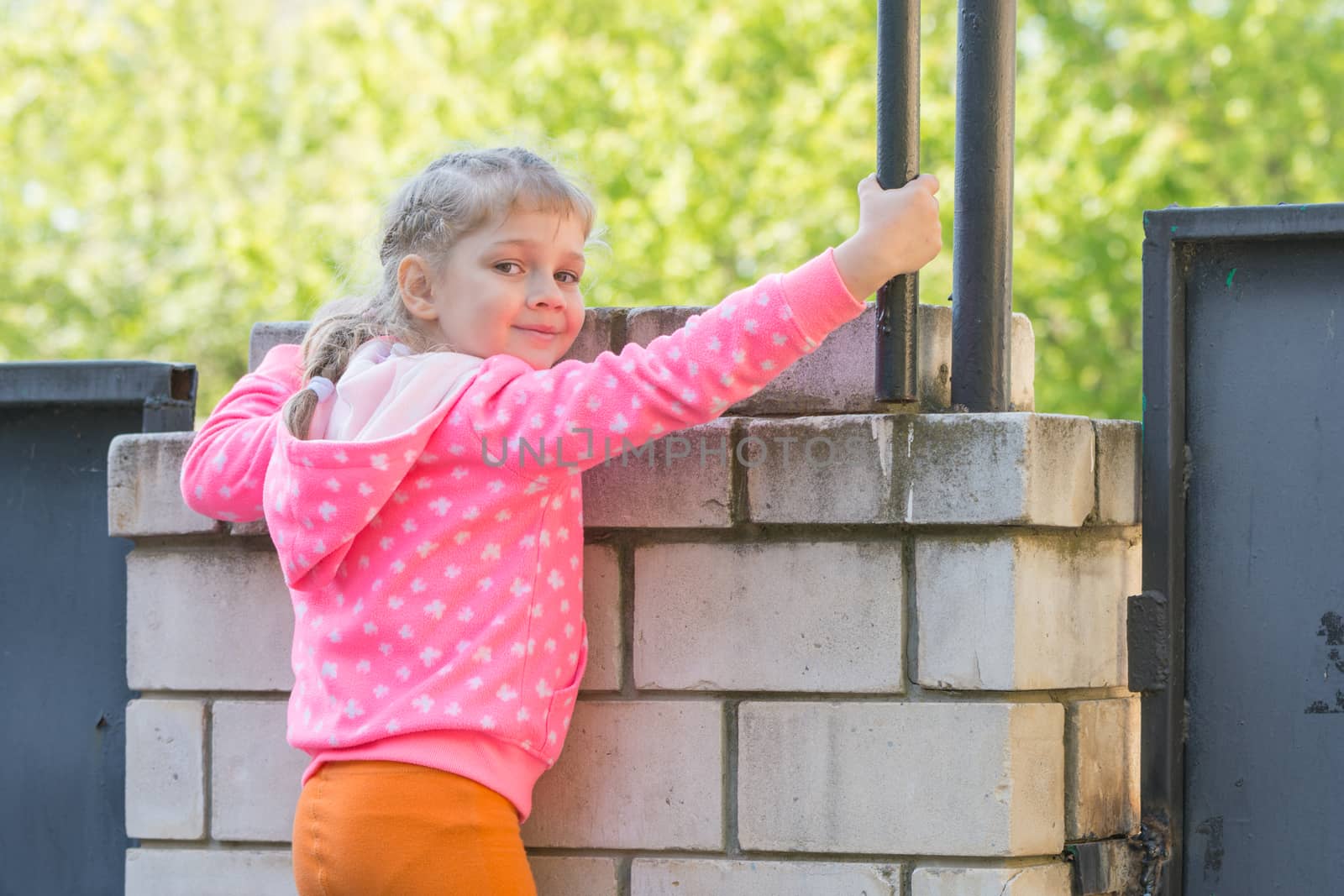 Five-year girl climbed on a brick fence and turned around looked at the frame