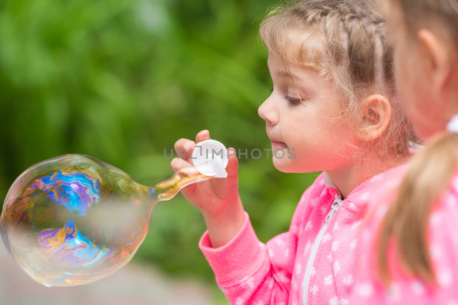 Five-year girl inflates a large bubble, another girl with interest looks at her
