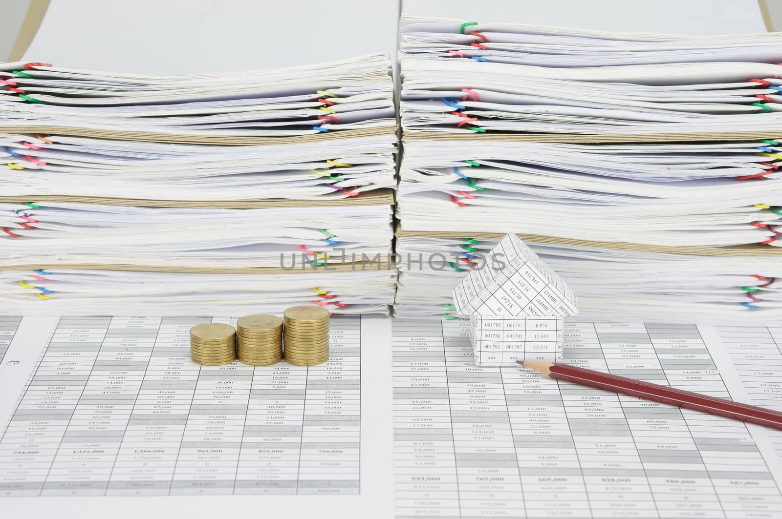 House and brown pencil with step pile of gold coins on finance account have overload of paperwork with colorful paperclip and envelope as background.