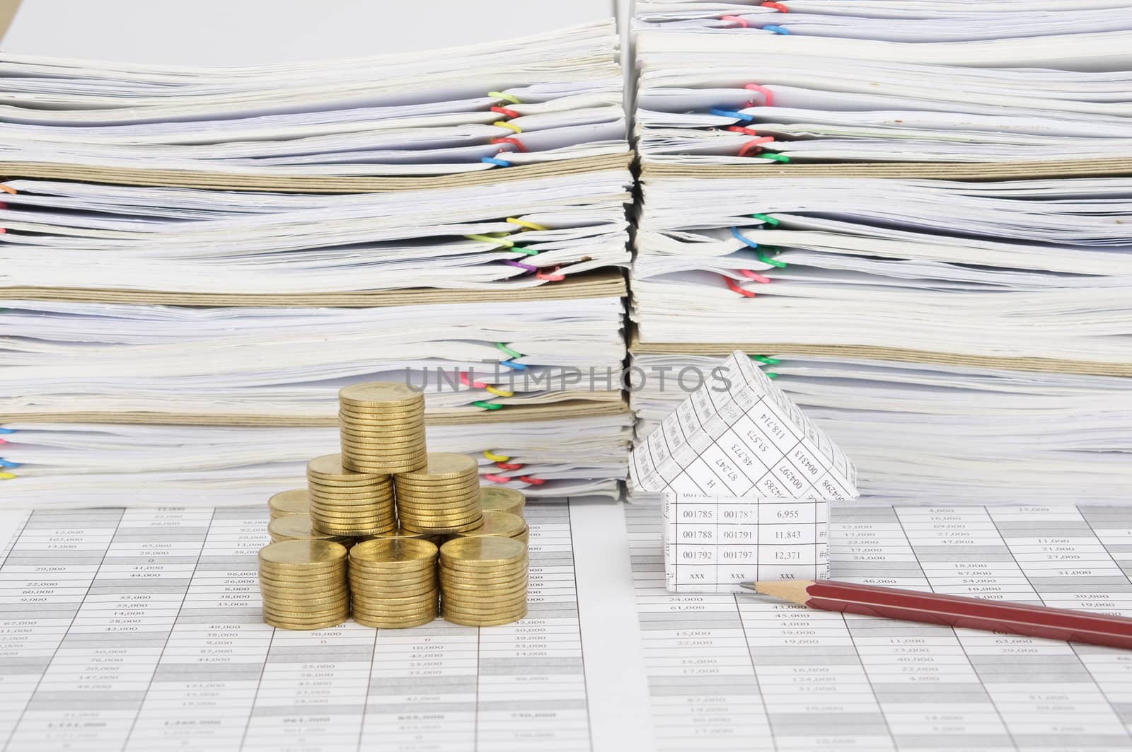 House and brown pencil with stack of gold coins as tower on finance account have overload of paperwork with colorful paperclip and envelope as background.