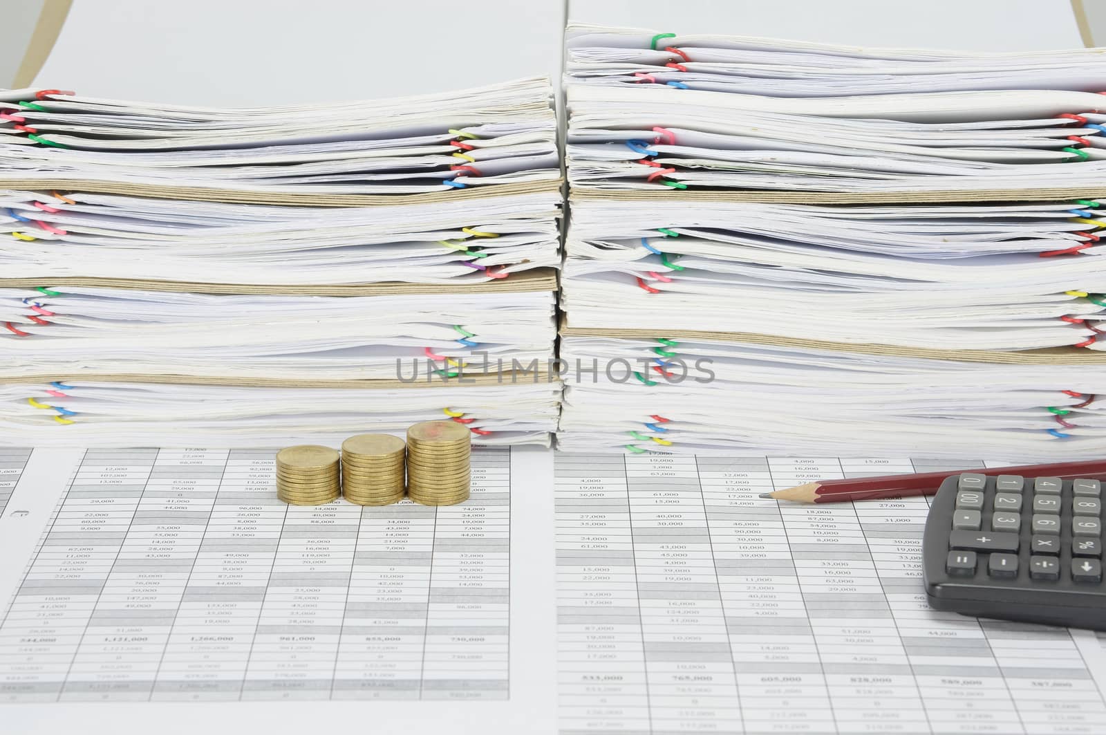 Brown pencil with step pile of gold coins on finance account have overload of paperwork with colorful paperclip and envelope with calculator as background.