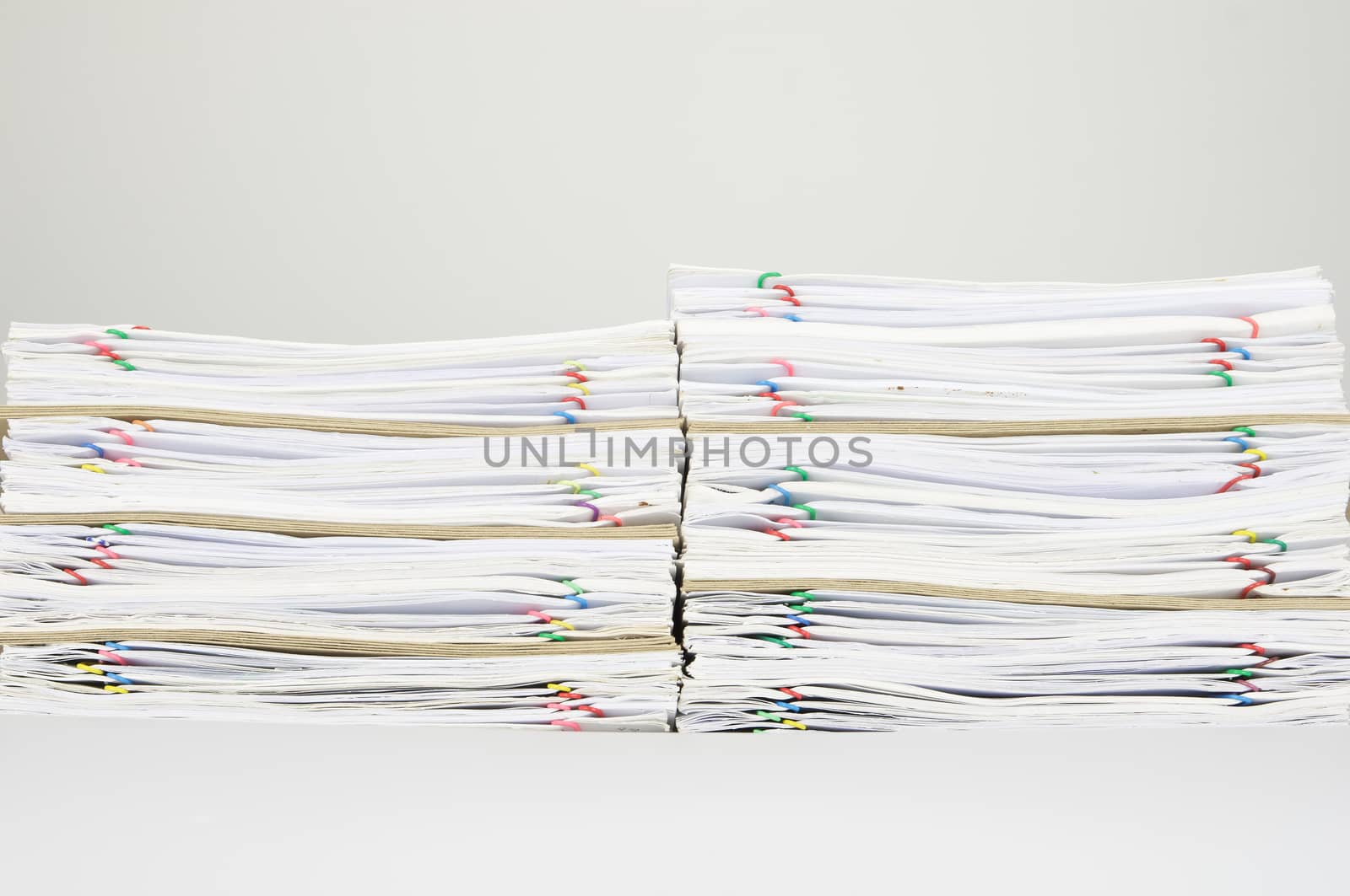 Pile of overload paperwork with colorful paperclip and envelope on white background.