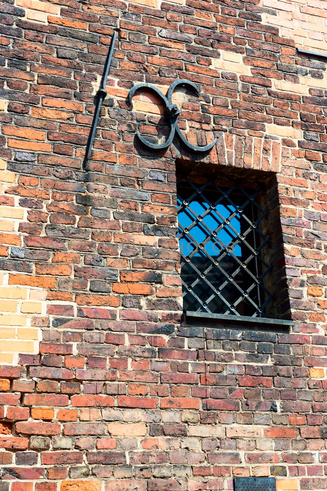 Small barred window in an old brick wall. The metal bars of the window in the form of an arch