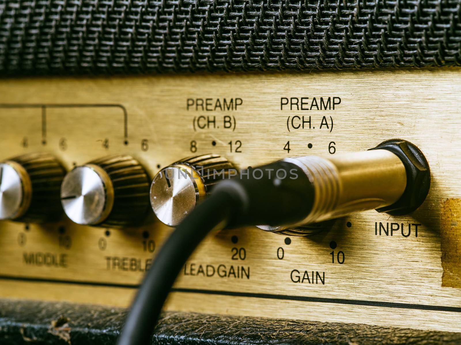 Macro photo of a vintage electric guitar amplifier showing the knobs and input plug.
