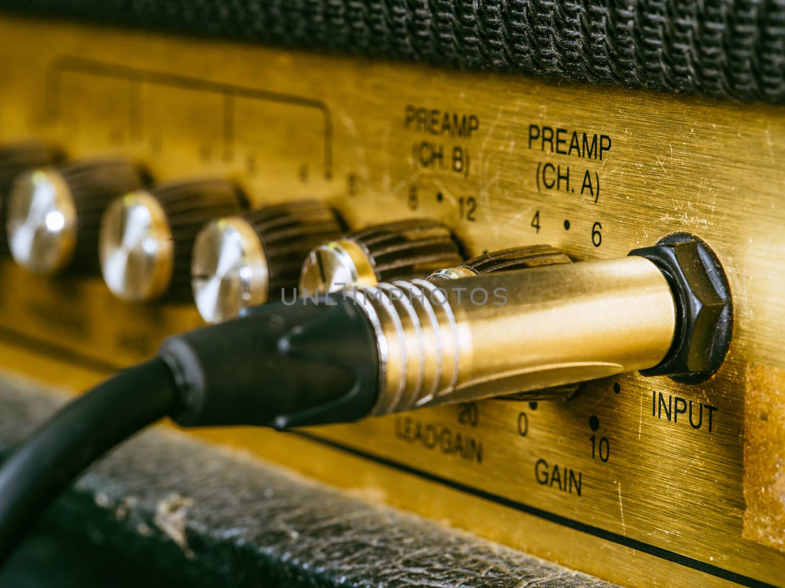 Macro photo of a vintage electric guitar amplifier showing the knobs and input plug. Selective focus on the word input.