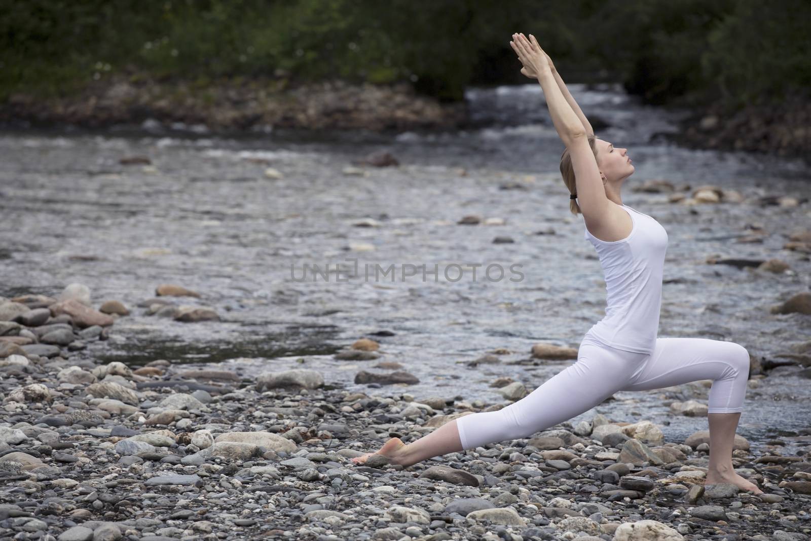 Young woman is practicing yoga at stone shore river