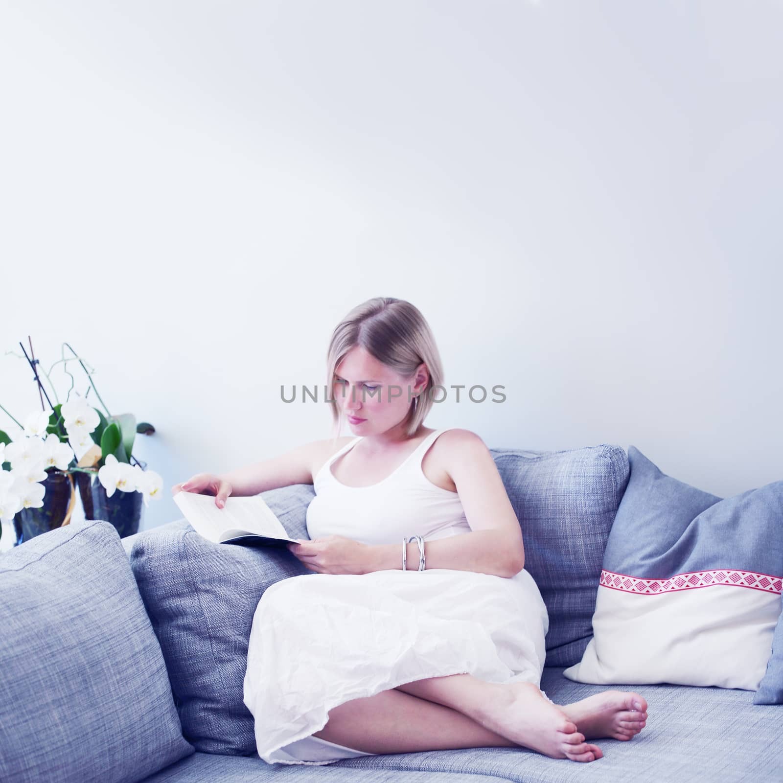 Happy young woman reading book on couch at home