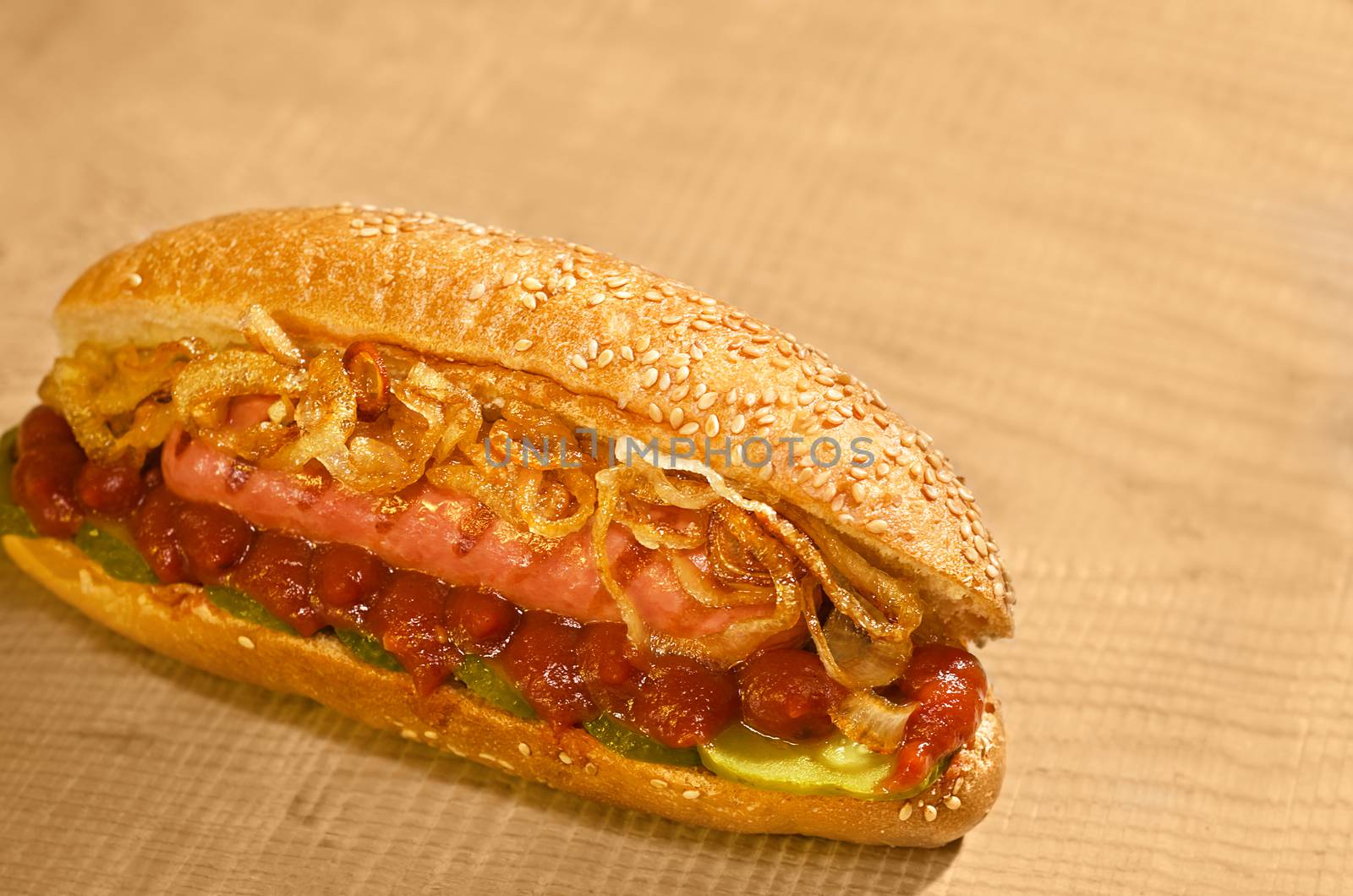 Hot dog with pickles, ketchup and grilled onions, laying on a Board. Warm color and bokeh.