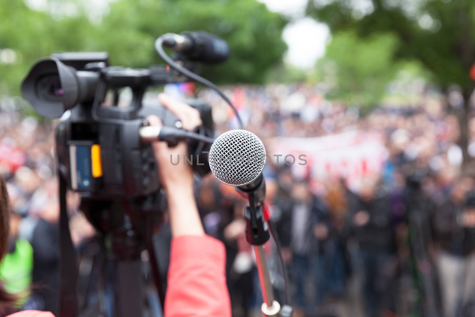 Microphone in focus against blurred crowd. Filming protest. by wellphoto