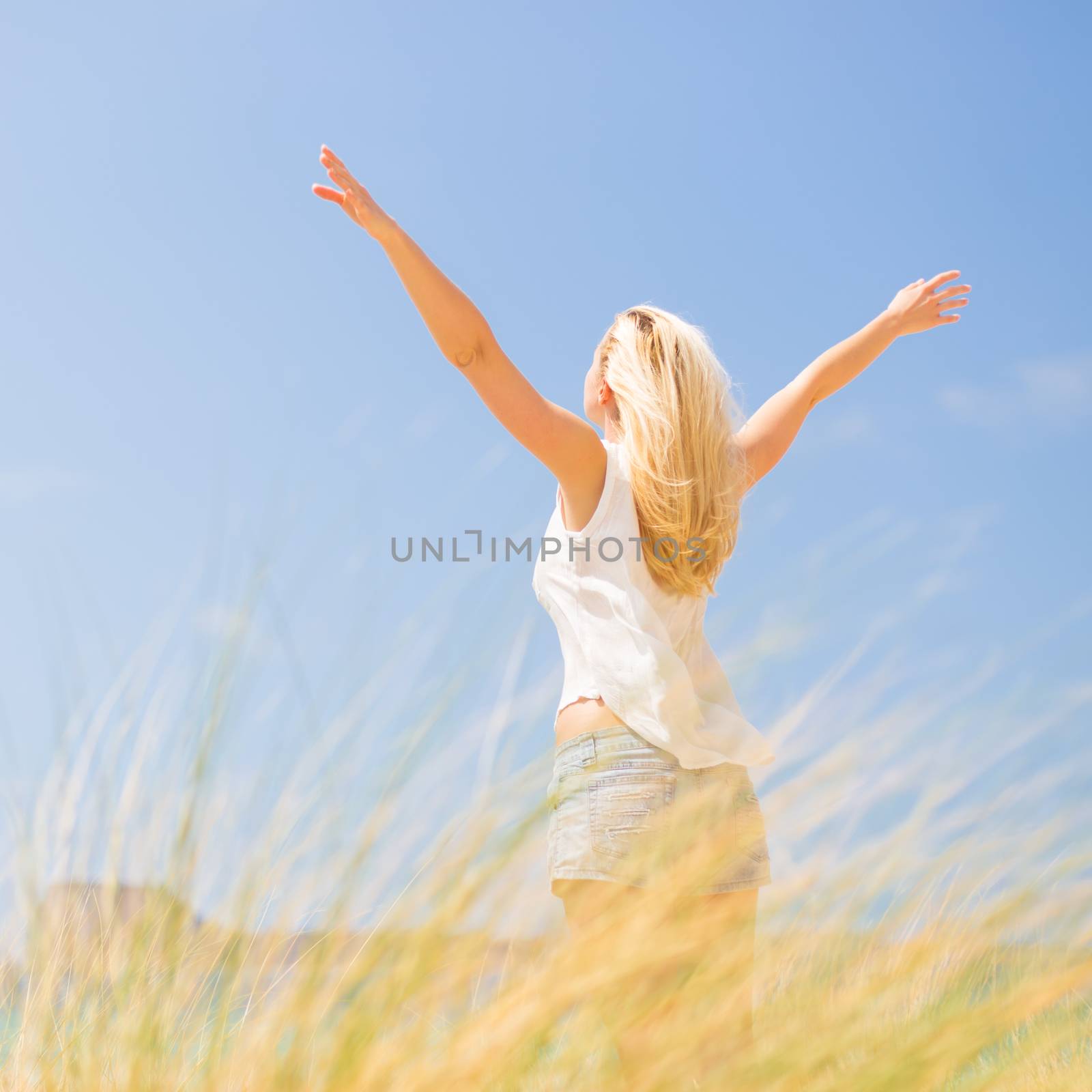 Relaxed woman, arms rised, enjoying sun, freedom and life an a beautiful beach. Young lady feeling free, relaxed and happy. Concept of vacations, freedom, happiness, enjoyment and well being.