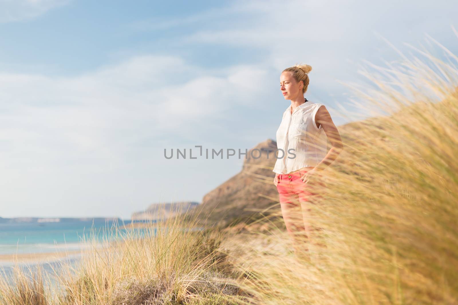 Relaxed woman enjoying sun, freedom and life an a beautiful sandy beach of Balos in Greece. Young lady feeling free, relaxed and happy. Vacations, freedom, happiness, enjoyment and well being.