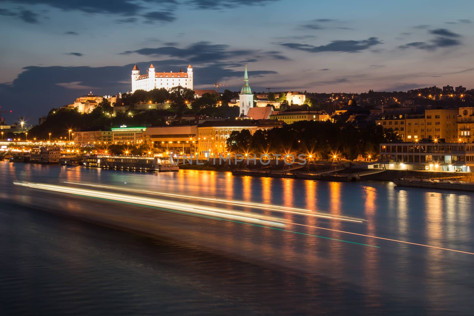 City Bratislava, capital of Slovak Republic. Night view on the river Danube with a passing boat, cathedral in the old city and the castle.