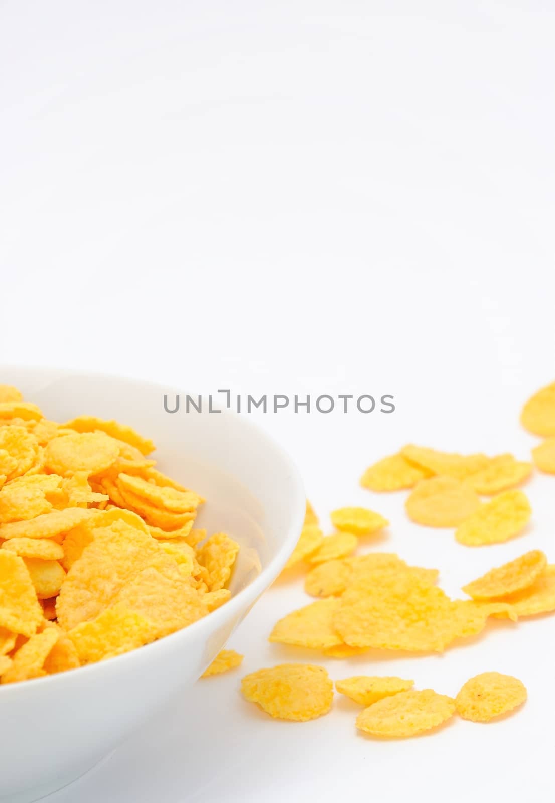 Gold corn flakes heaped in the white dish and on the white table.