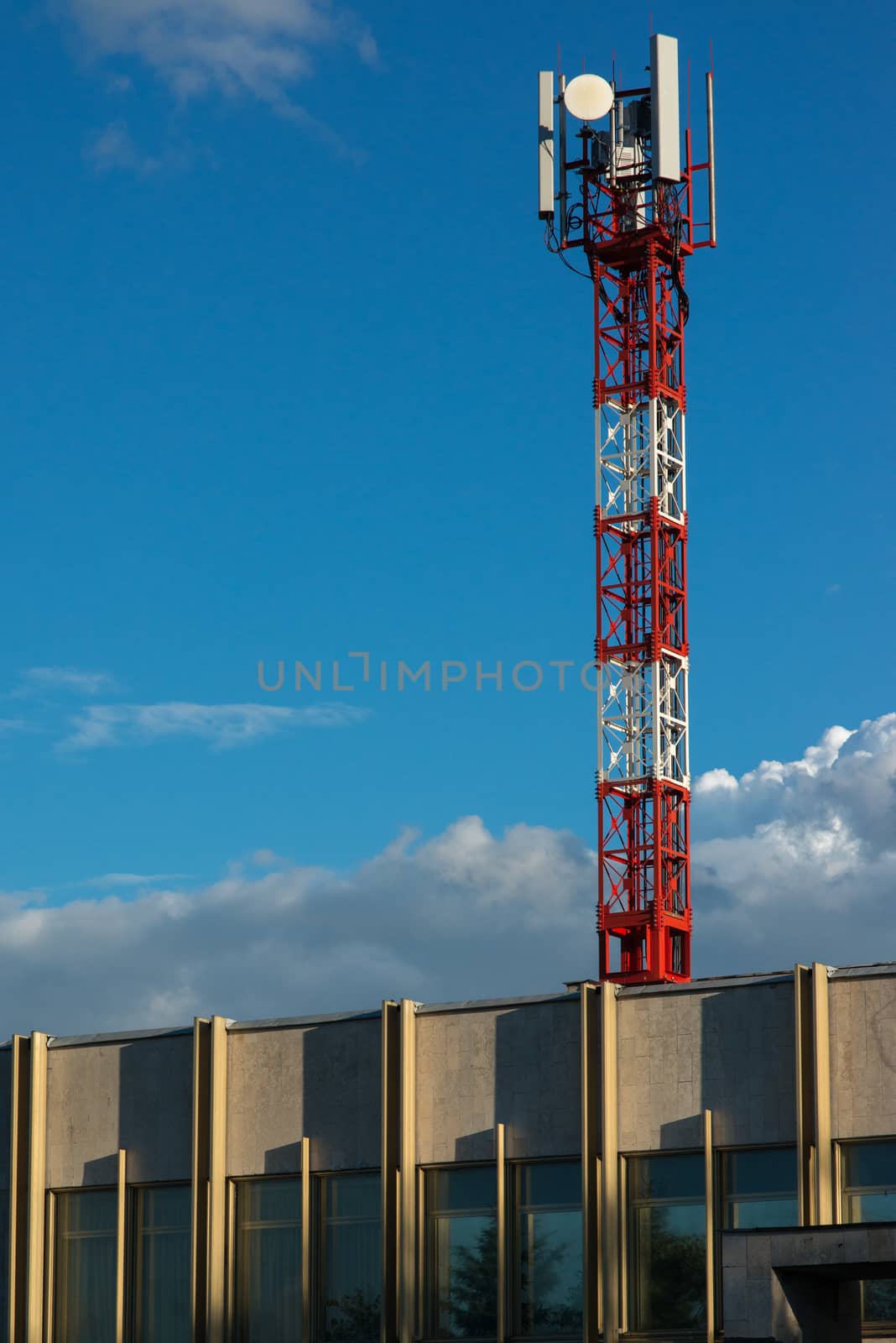 Red and white antenna tower on the roof of the building by skrotov