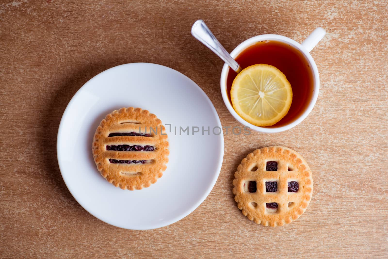 Cup of tea and lemon, cookies with jam in saucer on table top view.