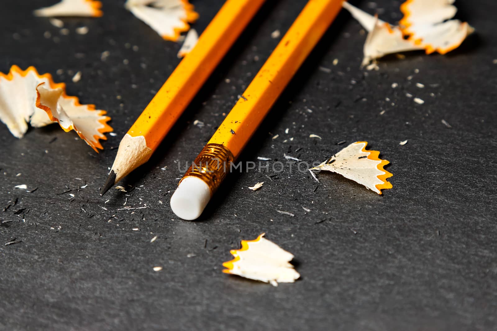 Two pencils with shavings on black background. Horizontal image.