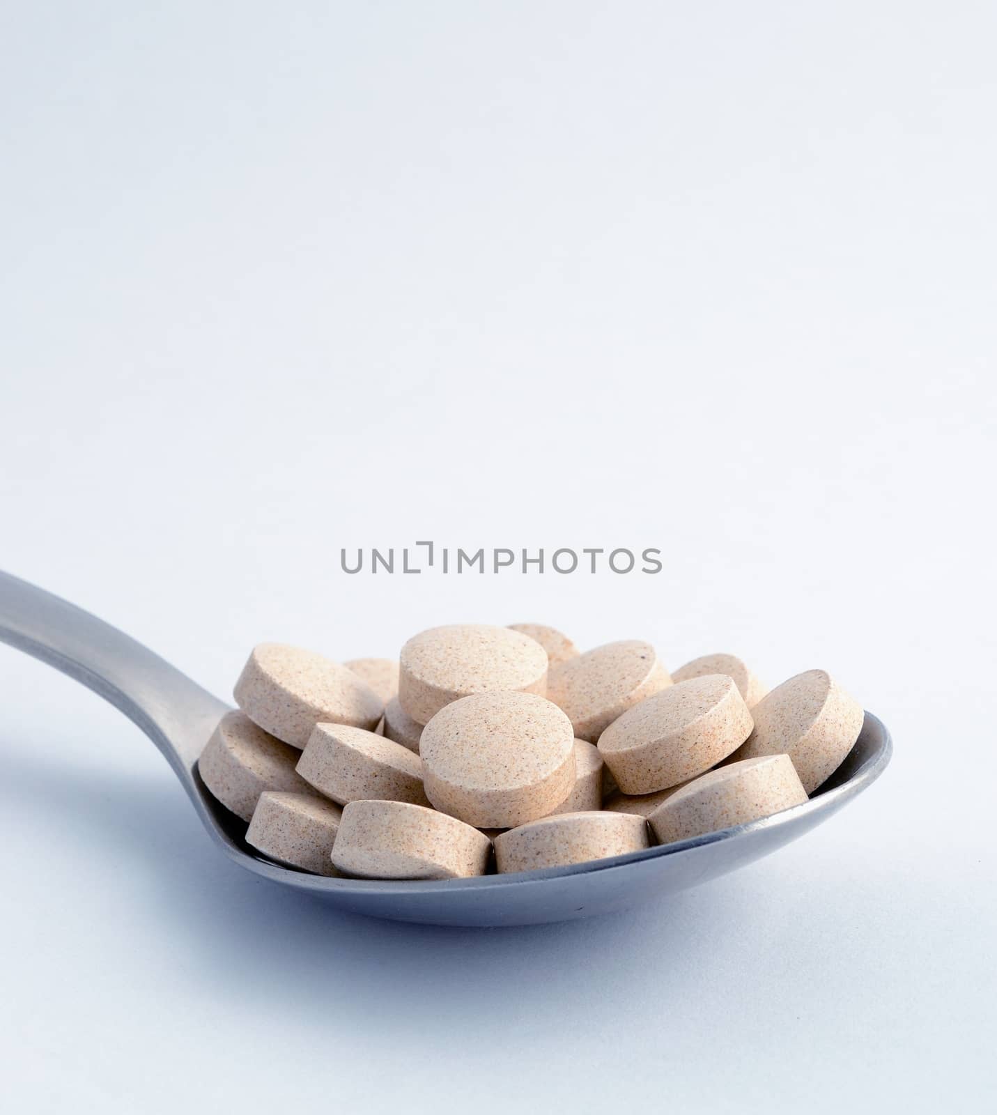 Macro shot of brown tablets at the spoon, grey background. 