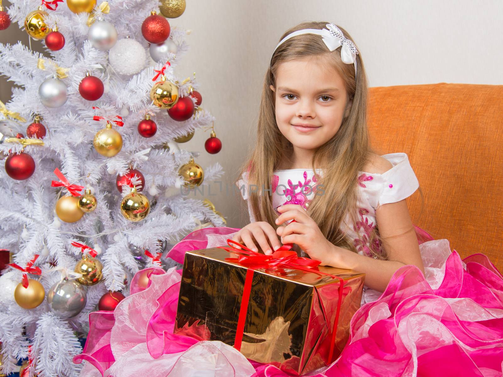 Seven-year girl in a beautiful dress sits with a gift in their hands