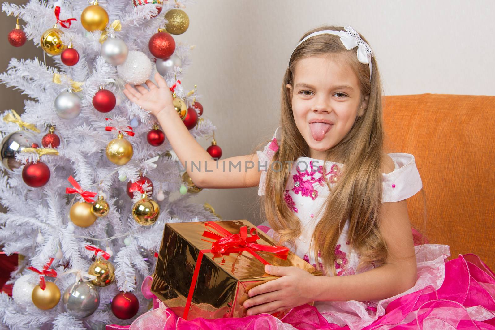 Seven-year girl in a beautiful dress sits with a gift and showed language to frame