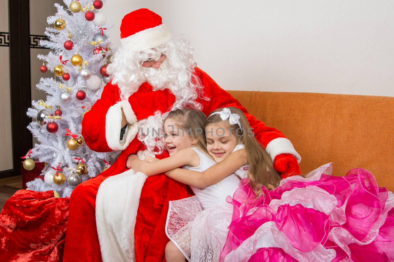 Two girls in beautiful dresses hug Santa Claus