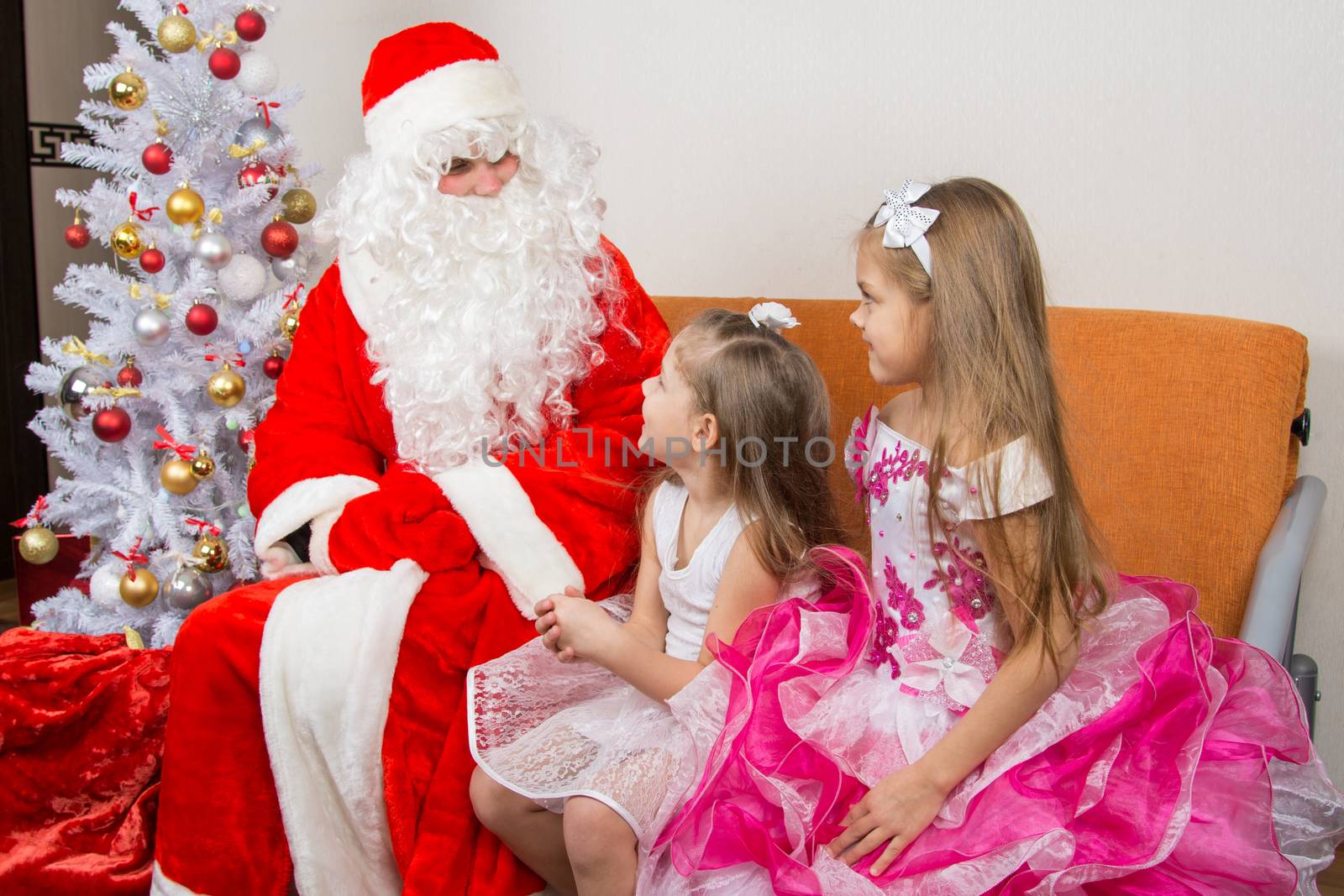 Two girls in beautiful dresses talk with Santa Claus