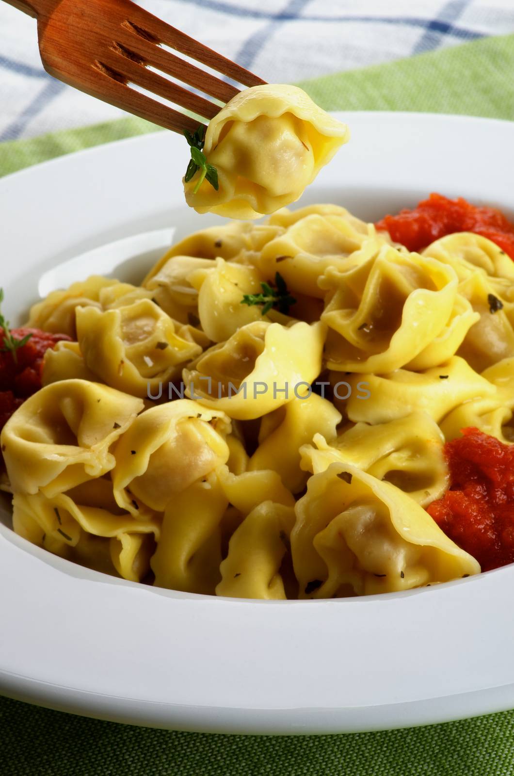 Delicious Meat Cappelletti in with Tomatoes Sauce and One on Wooden Fork closeup on Green Napkin background