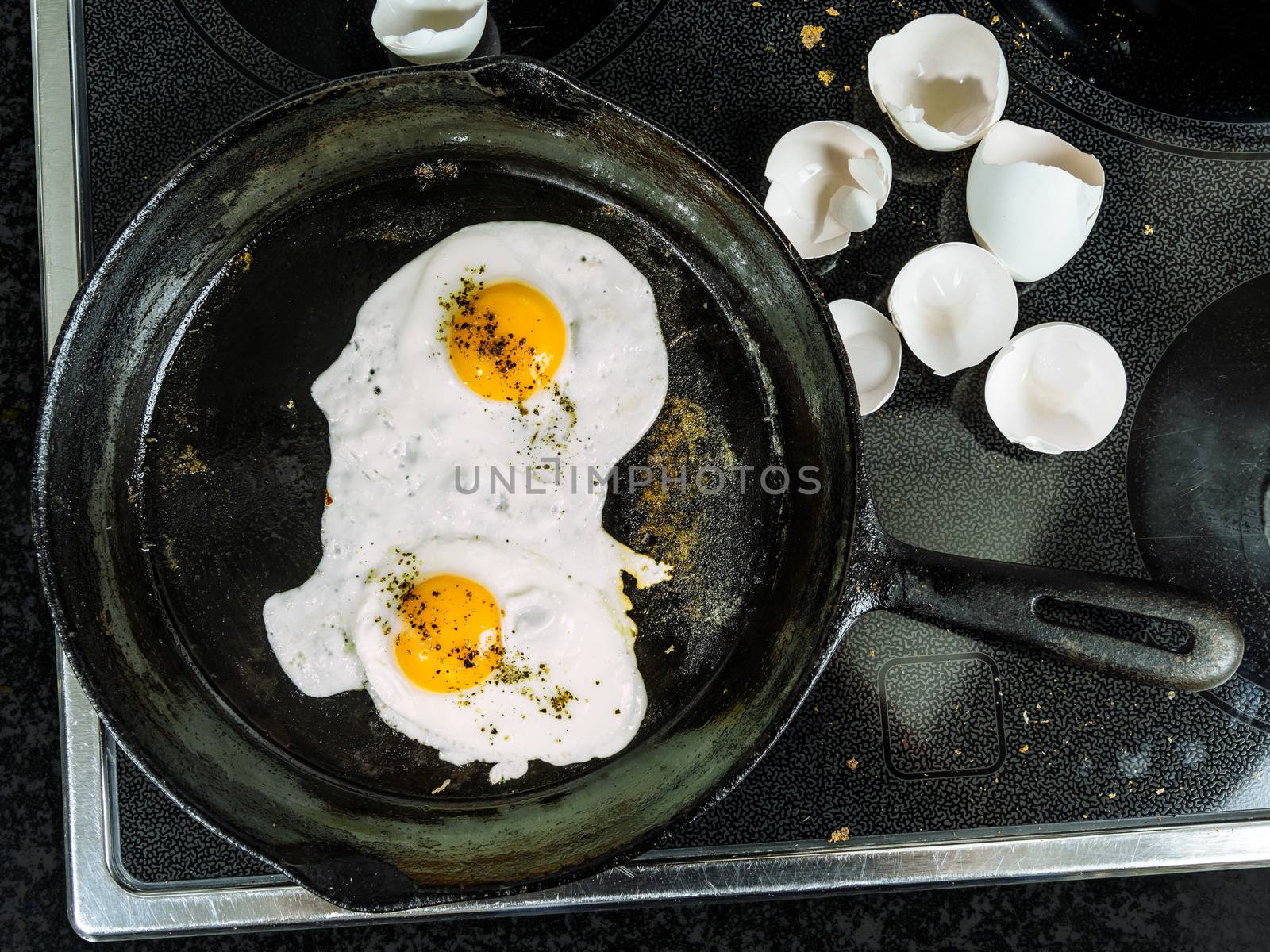 Photo of two eggs frying in a cast iron skillet on top of a stove with egg shells to the side.