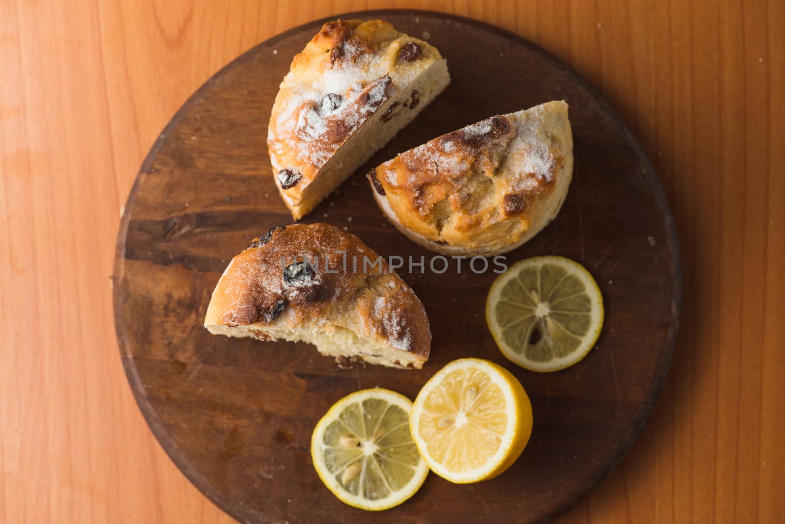 Top view of muffin with lemon in cup and on wooden plank table.