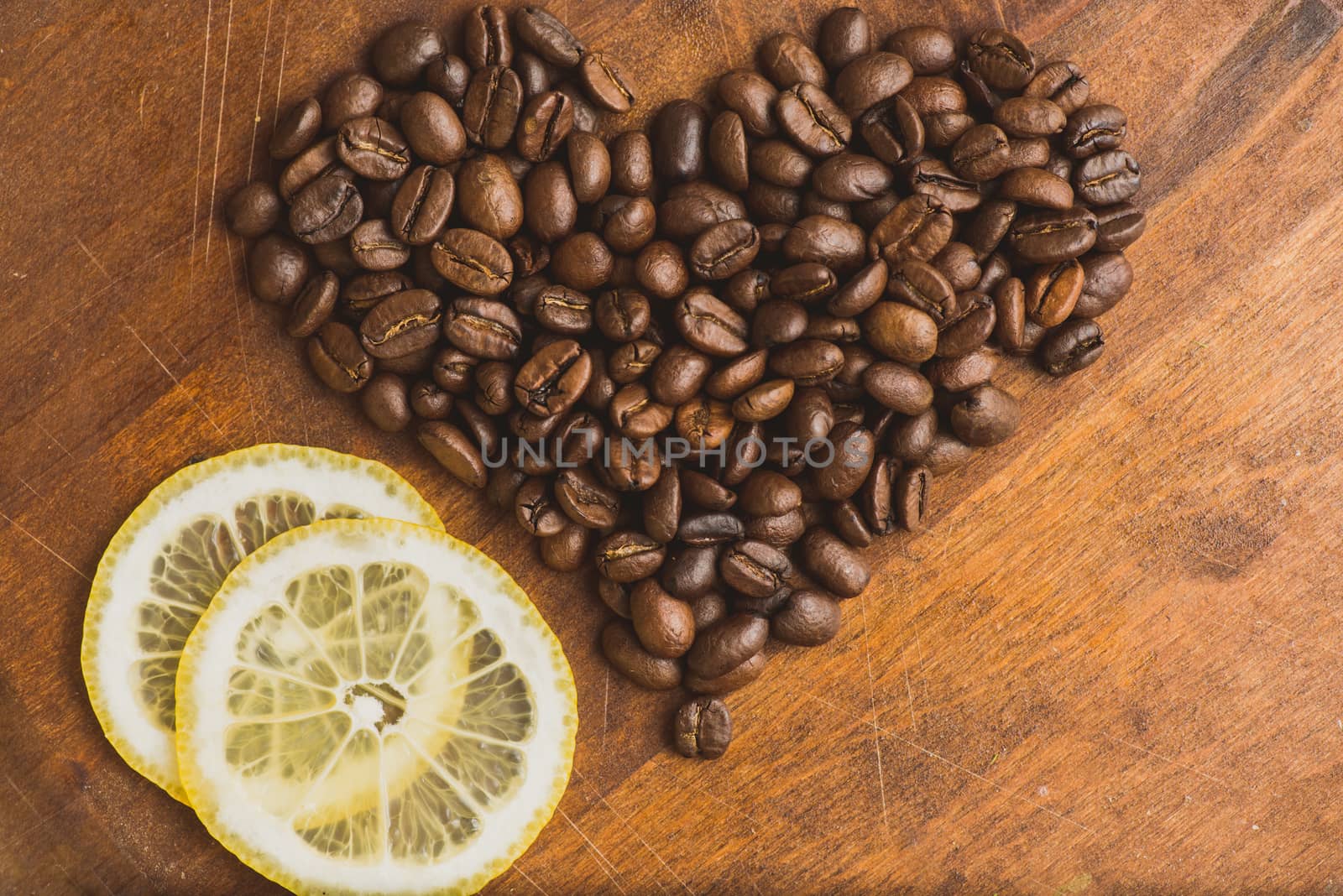 Brown coffee beans in shape of heart with lemon, closeup of macro coffee beans for background and texture. On brown wooden board.