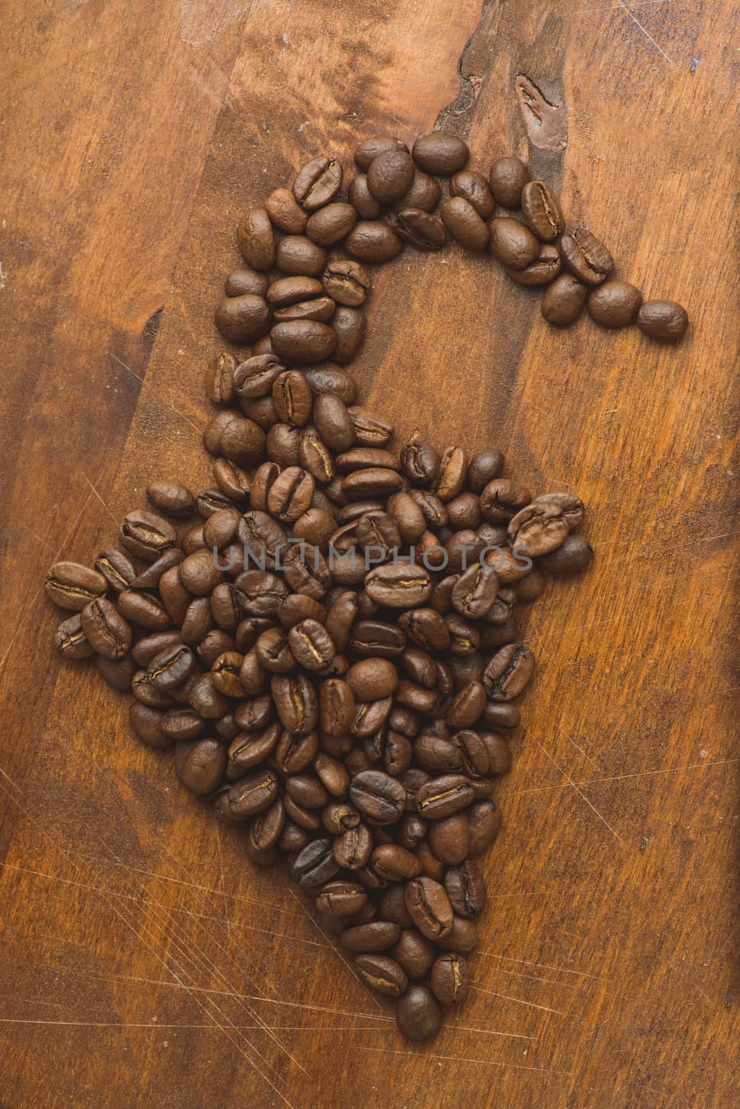Brown coffee beans in shape of pepper, closeup of macro coffee beans for background and texture. On brown wooden board