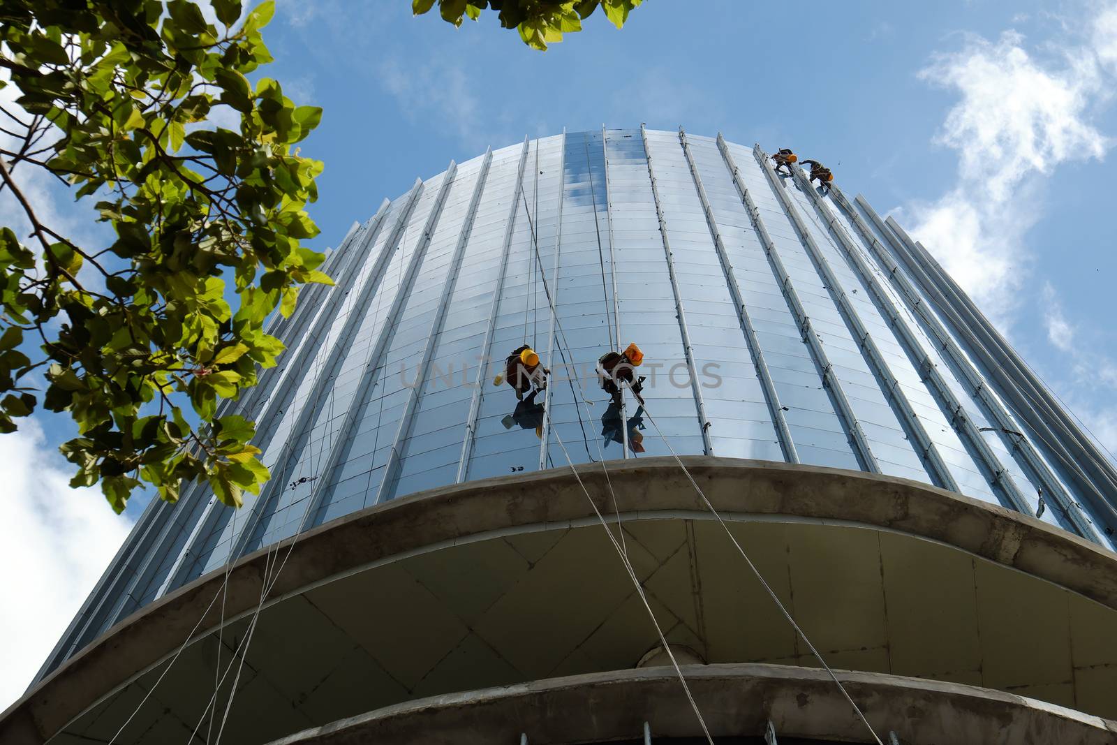 Group of Asian construction worker working on highrise building, Vietnamese man climb on rope and clean glass surface of skyscraper, a dangerous job of industry service