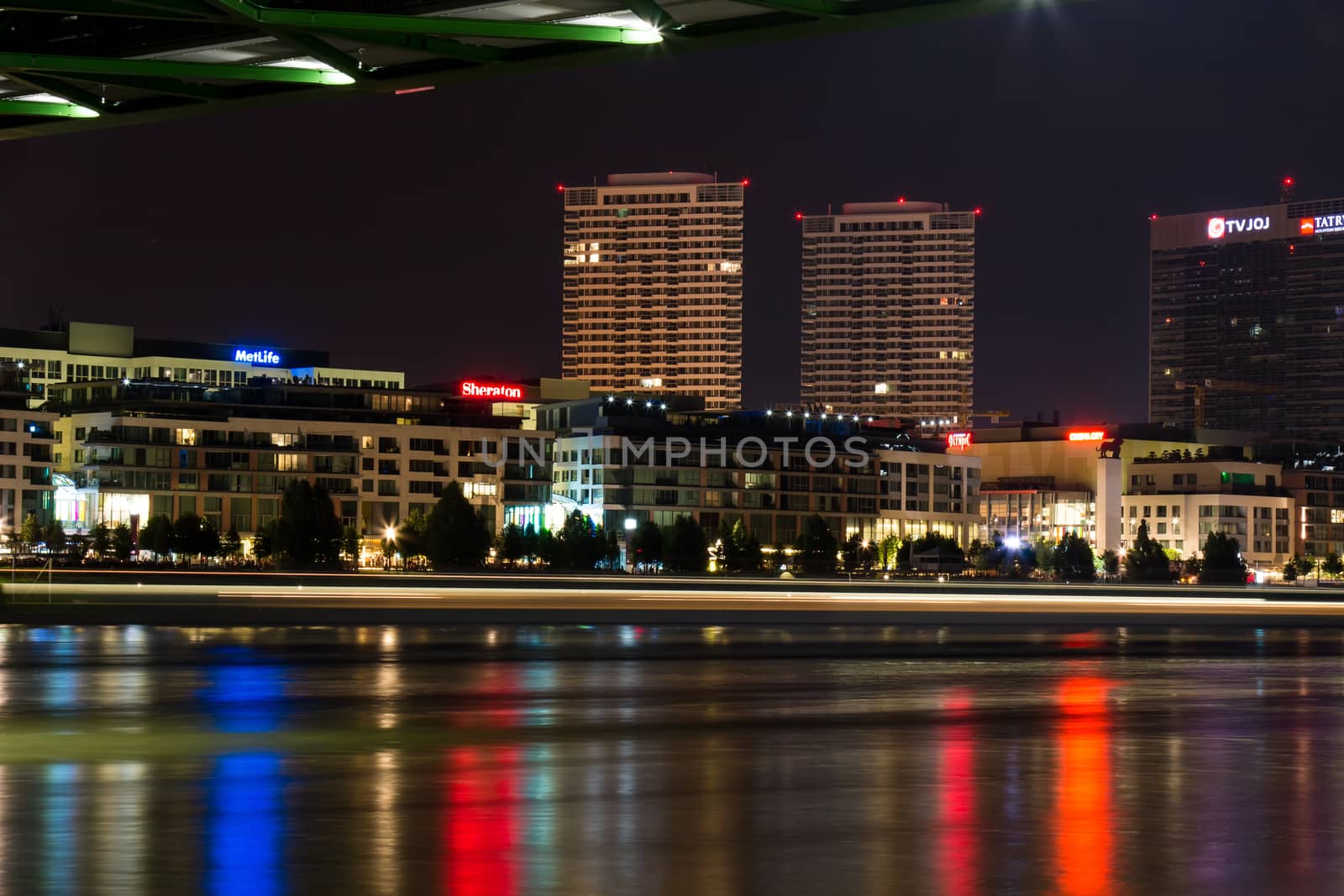 Night view from the riverbank of Danube on the new luxury part of Slovak capital - Bratislava. Lights line of a passing boat.