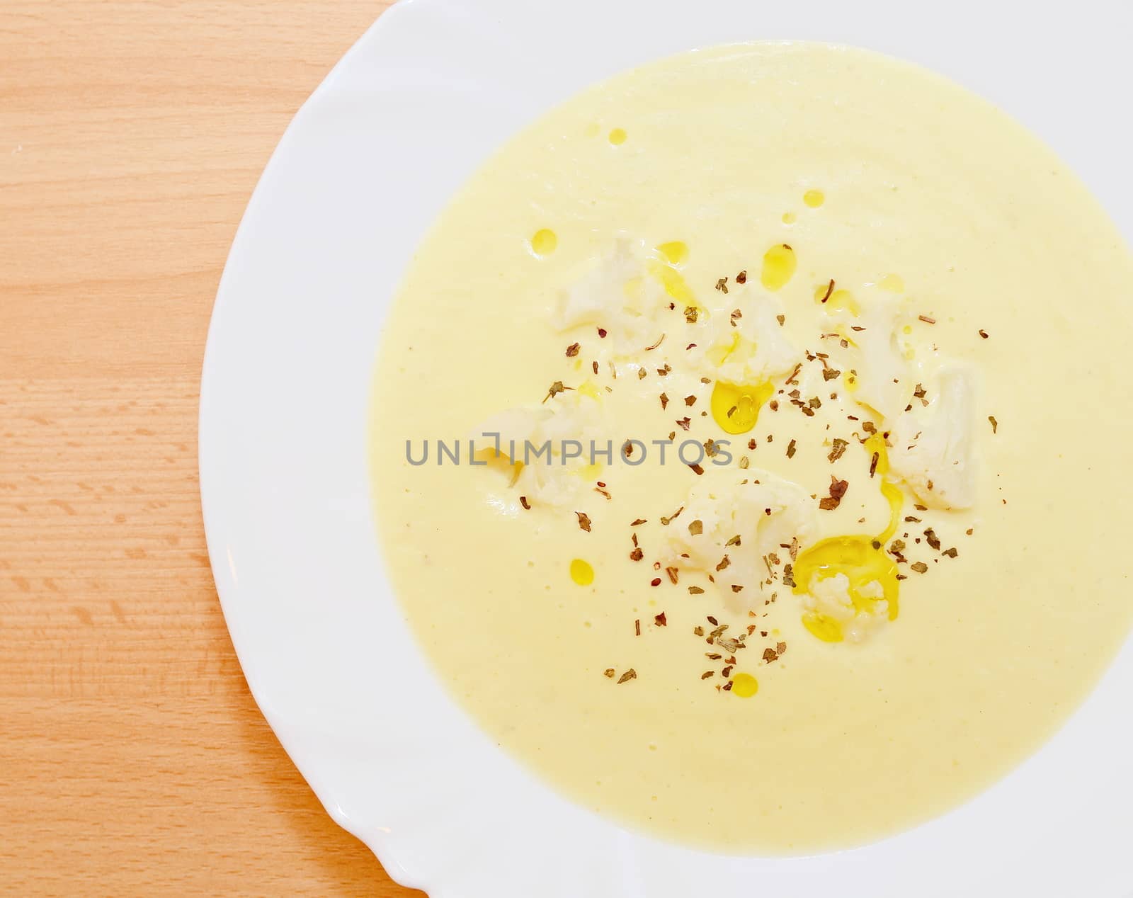 Top view on the table with cauliflower cream soup with olive oil, basil herbs and small whole cauliflowers.