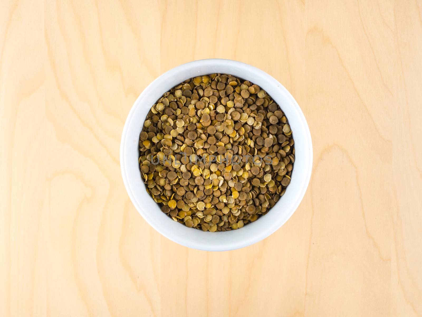 Pile of raw dry brown lentils in cup, top center by weruskak