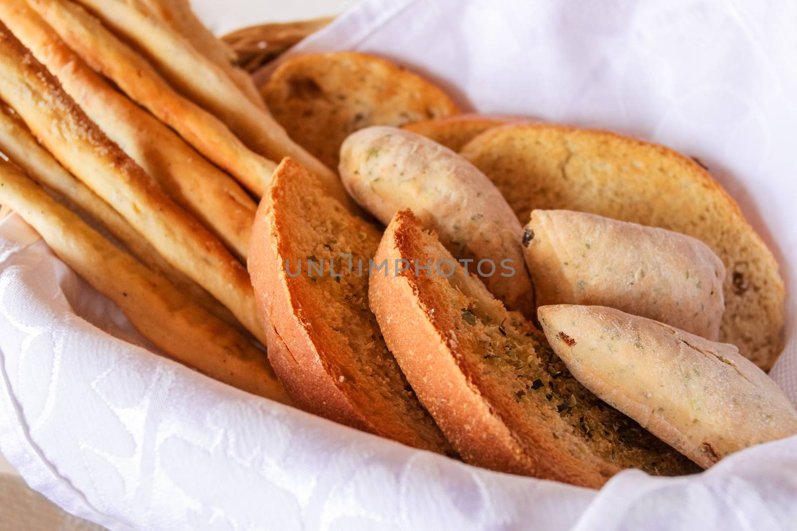 freshly backed various bread, tost, bagettes, served in a basket with white napkin.