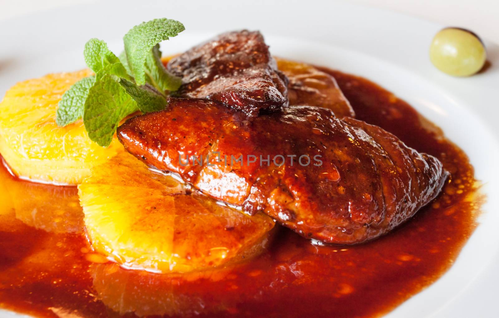 Luxuriously served roasted goose liver over orange slices with sauce and fresh mint meal.