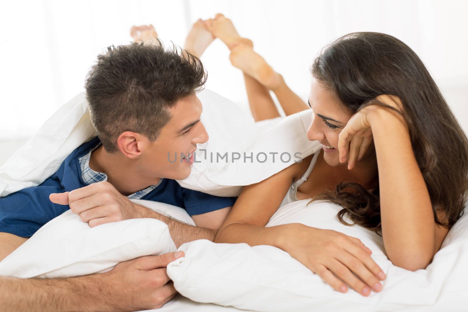 Beautiful young happy couple relaxing in bed and smiling.