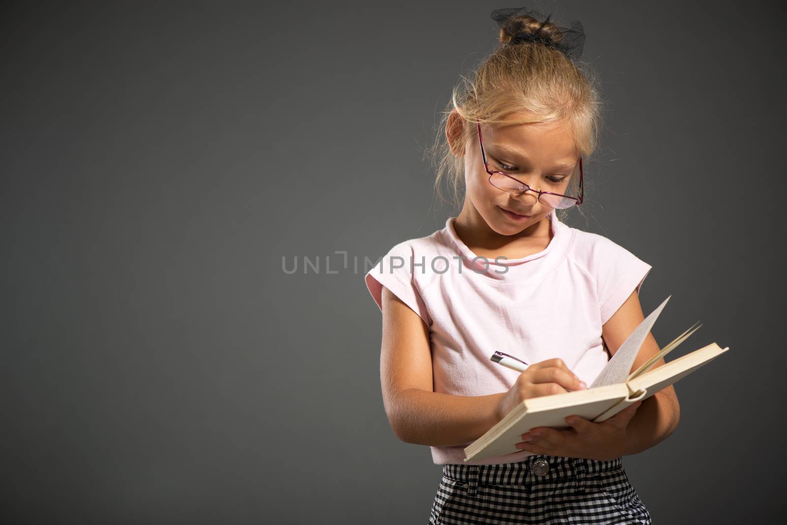 Tired Cute little girl standing and holding book. Studio shutting. Grey background. Looking at camera.
