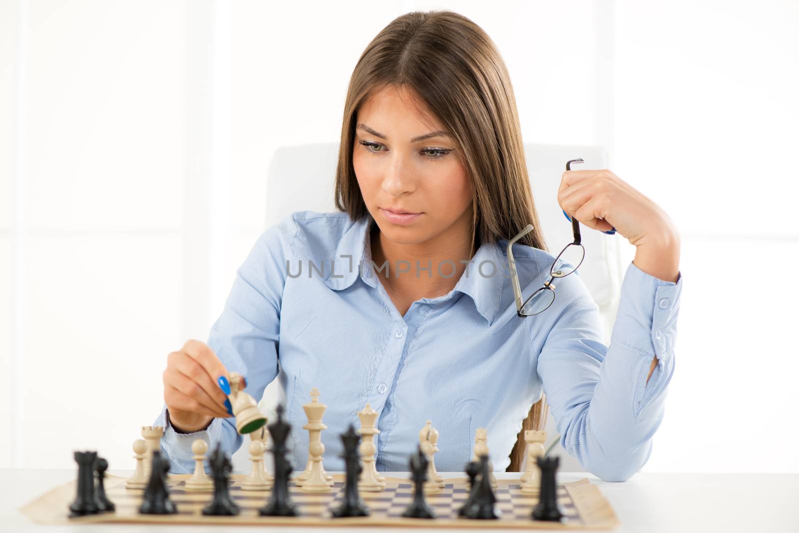 Young beautiful businesswoman devises Business strategy. She sitting above the chessboard with figures and thinking.