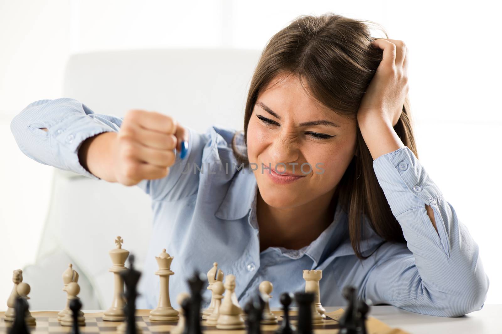 Angry businesswoman devises Business strategy. She sitting above the chessboard with figures and thinking.