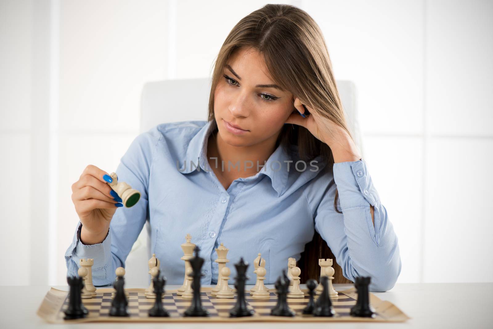 Young beautiful businesswoman devises Business strategy. She sitting above the chessboard with figures and thinking.
