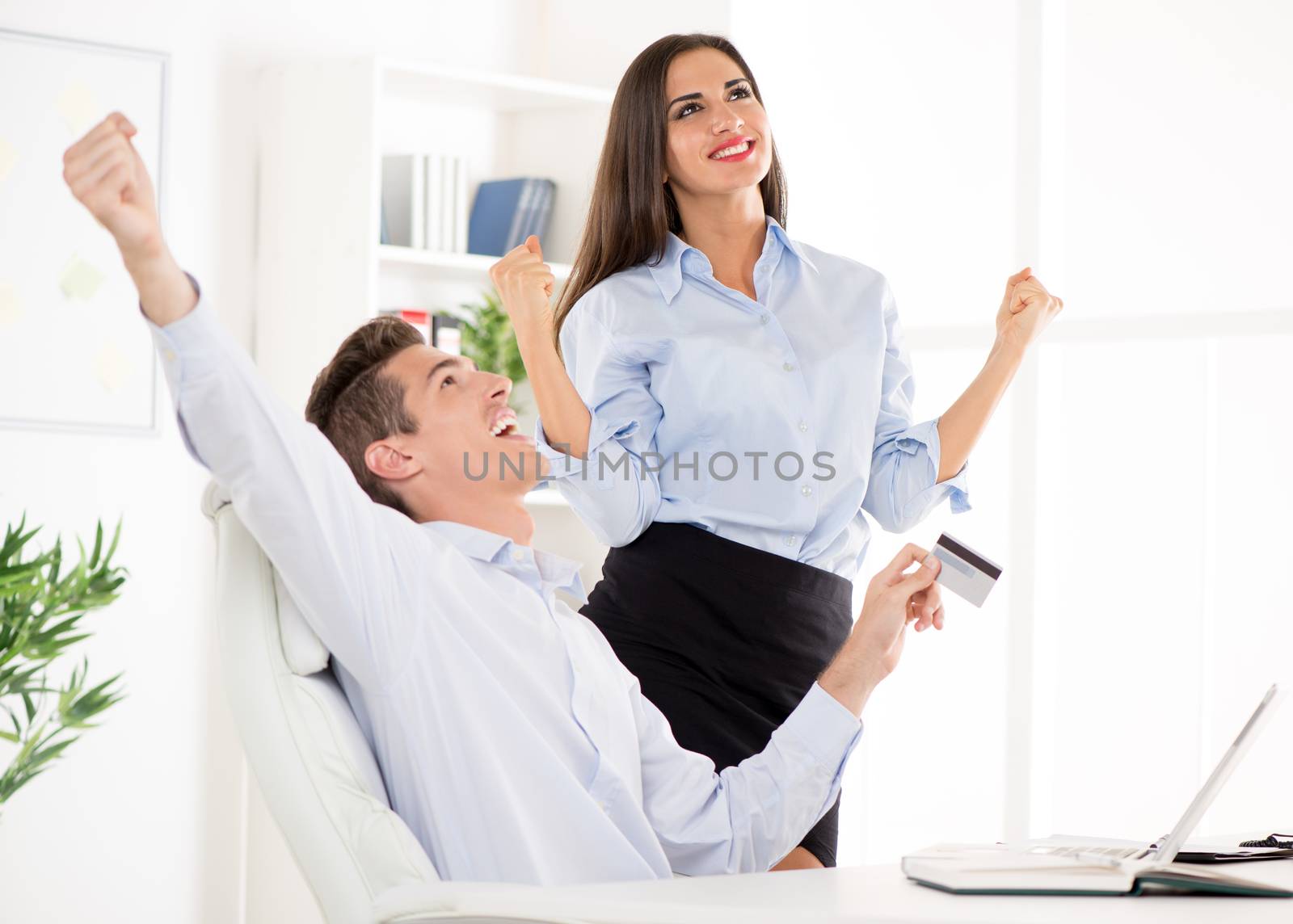 Successful Young businesswoman and businessman in the office with raised arms.