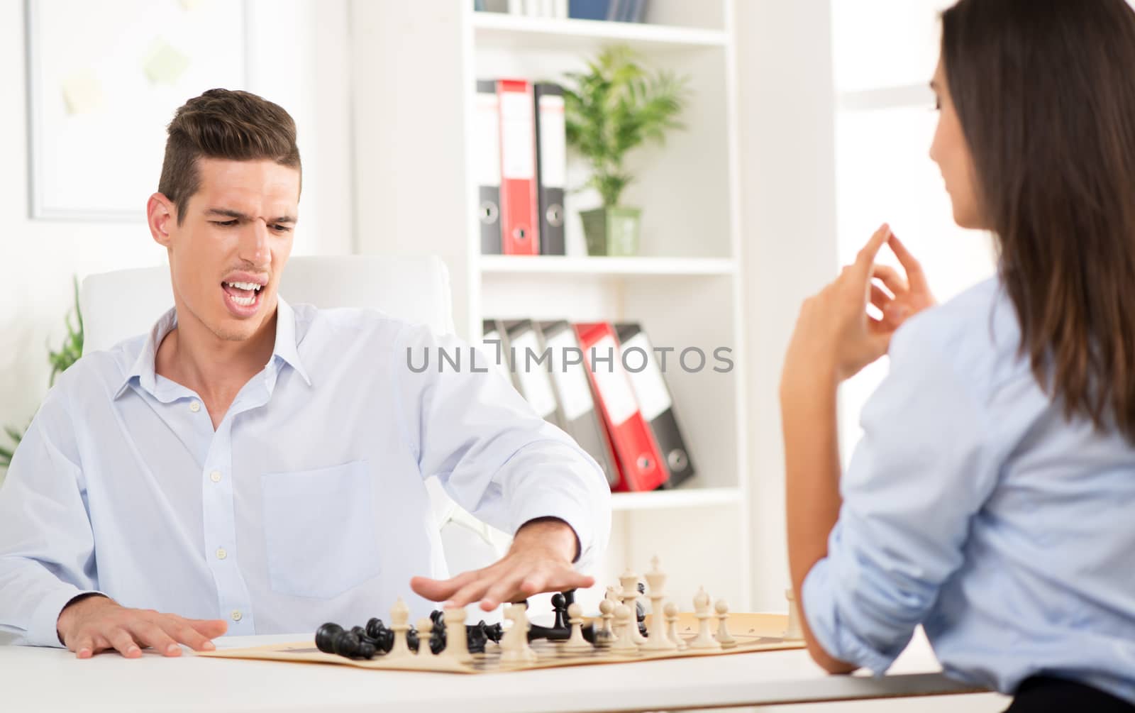 Young angry businessman of loses playing chess with businesswoman in the office.