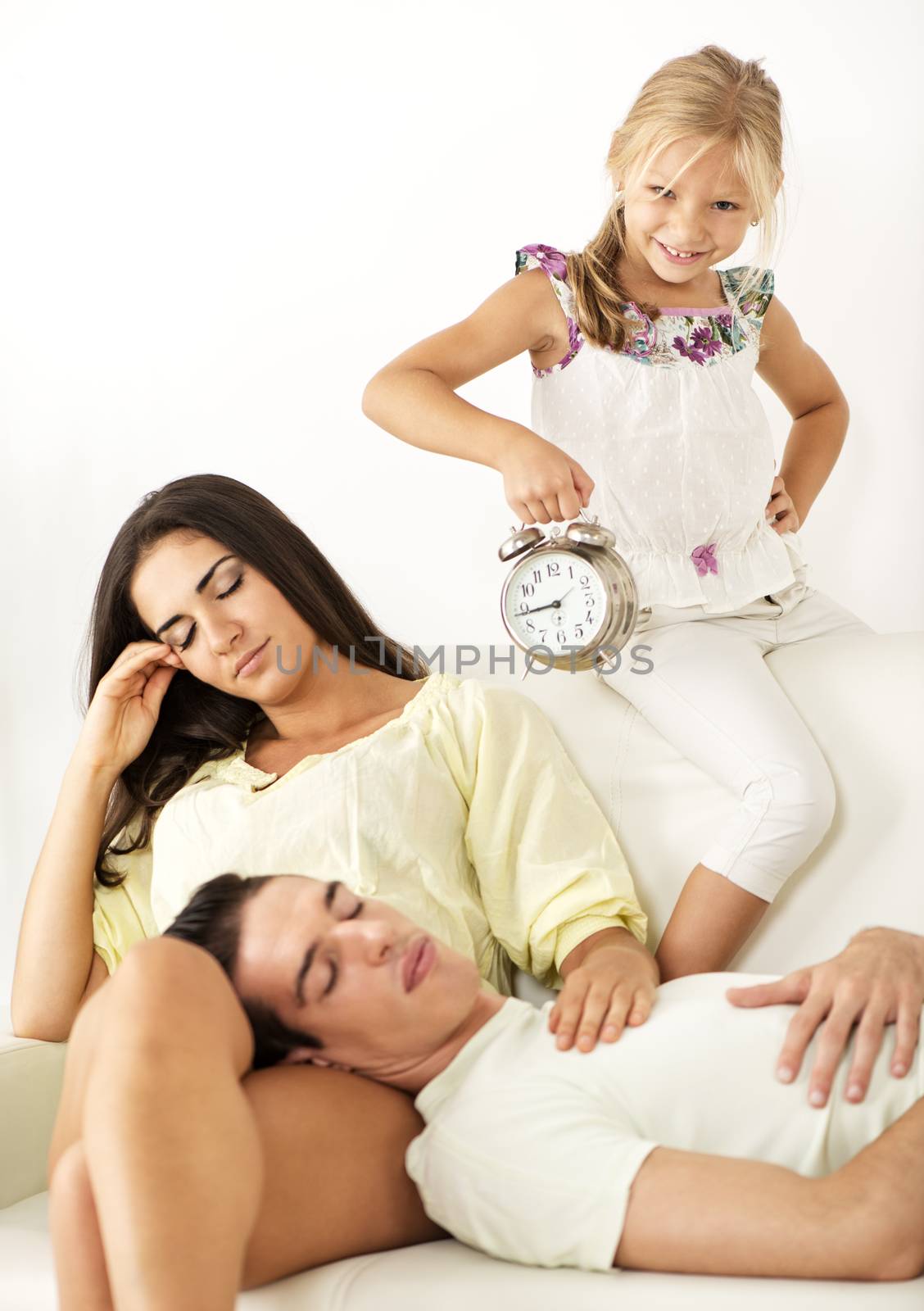 Cute little girl holding an alarm clock and waking up her parents