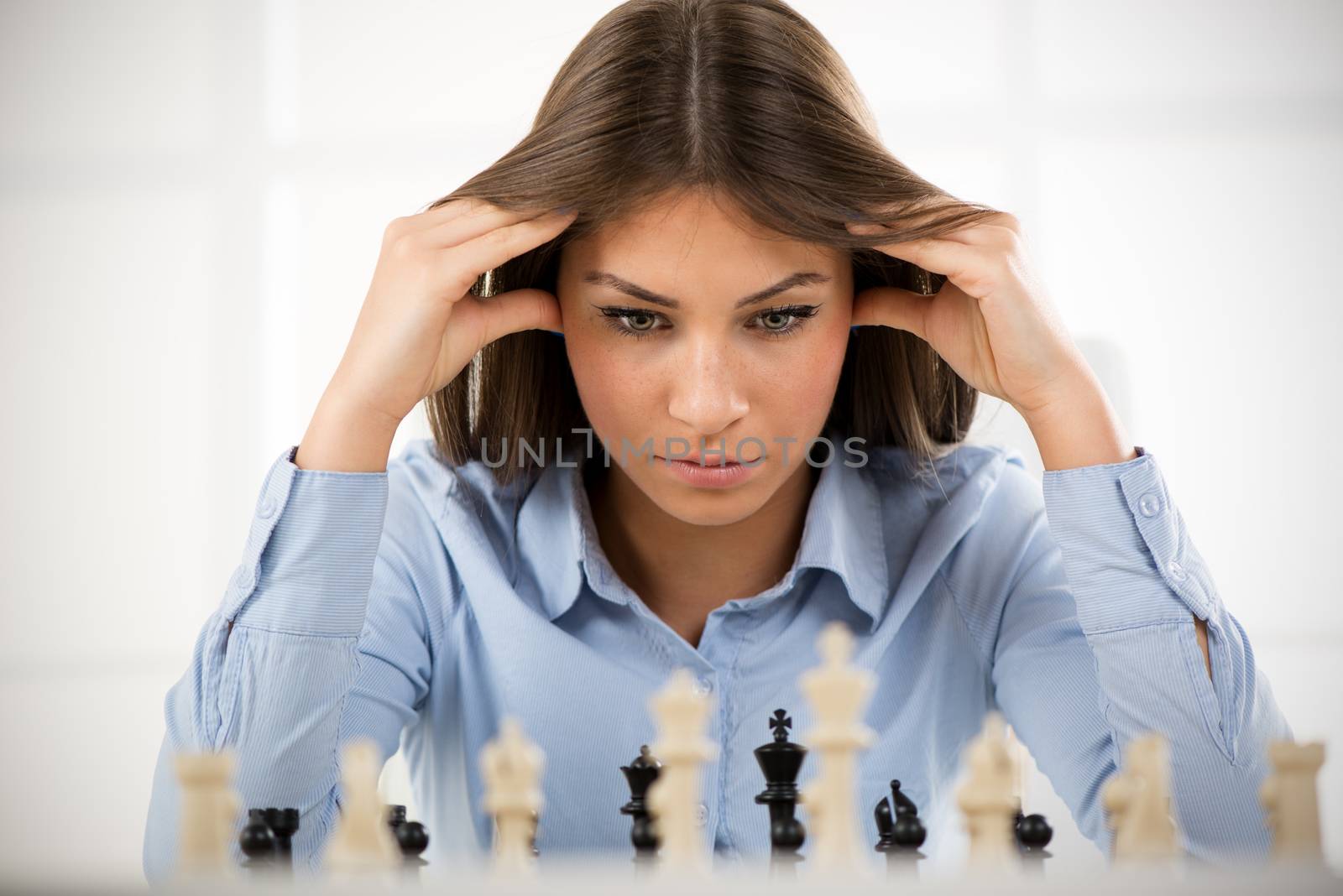 Young beautiful businesswoman devises Business strategy. She sitting above the chessboard with figures and thinking.