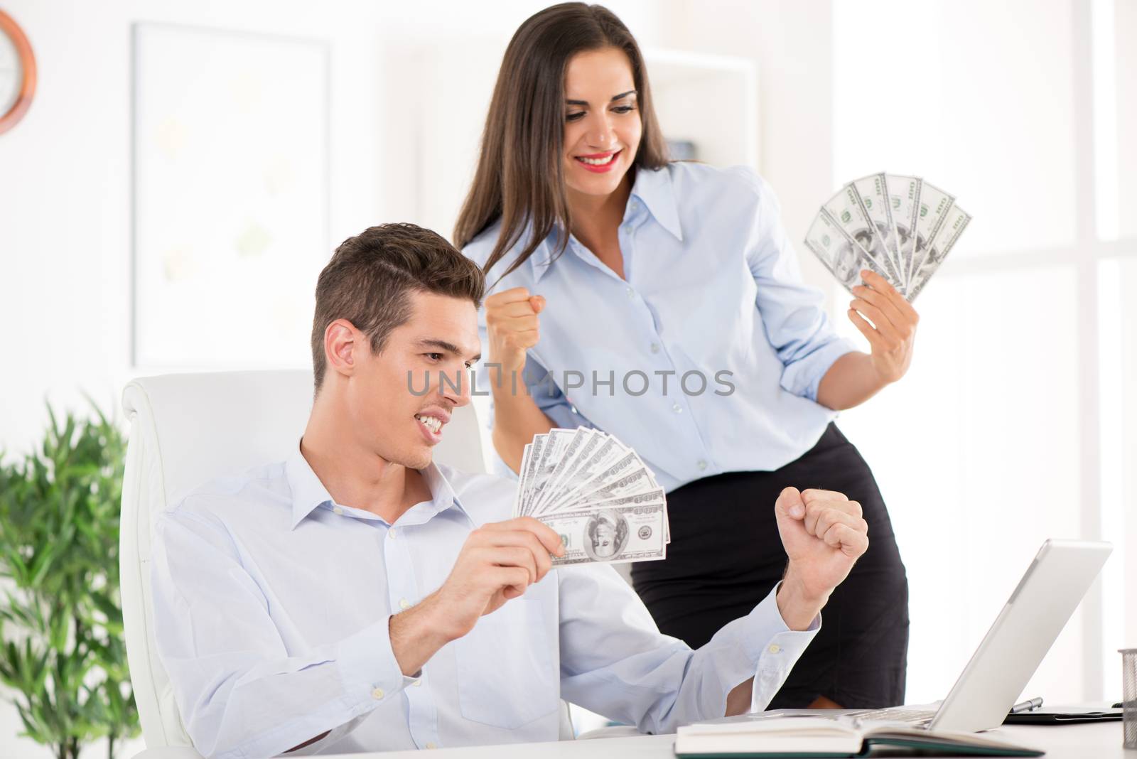 Happy successful Business team holding money and looking in laptop in the office.