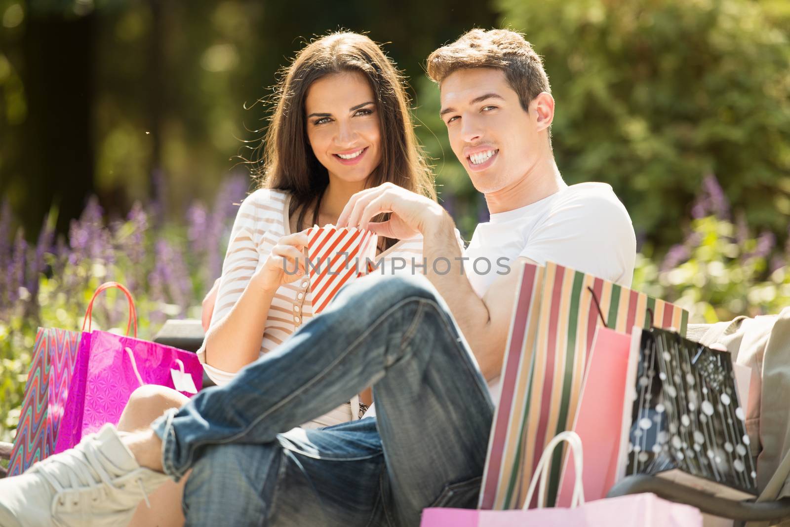 A young couple resting on a park bench after shopping, enjoying the autumn sun while nibbling popcorn.