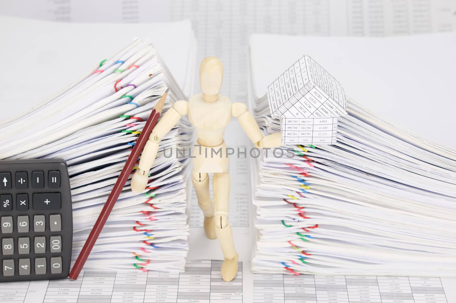 Wooden dummy holding house and pencil with calculator between dual pile overload document of report with colorful paperclip on finance account.