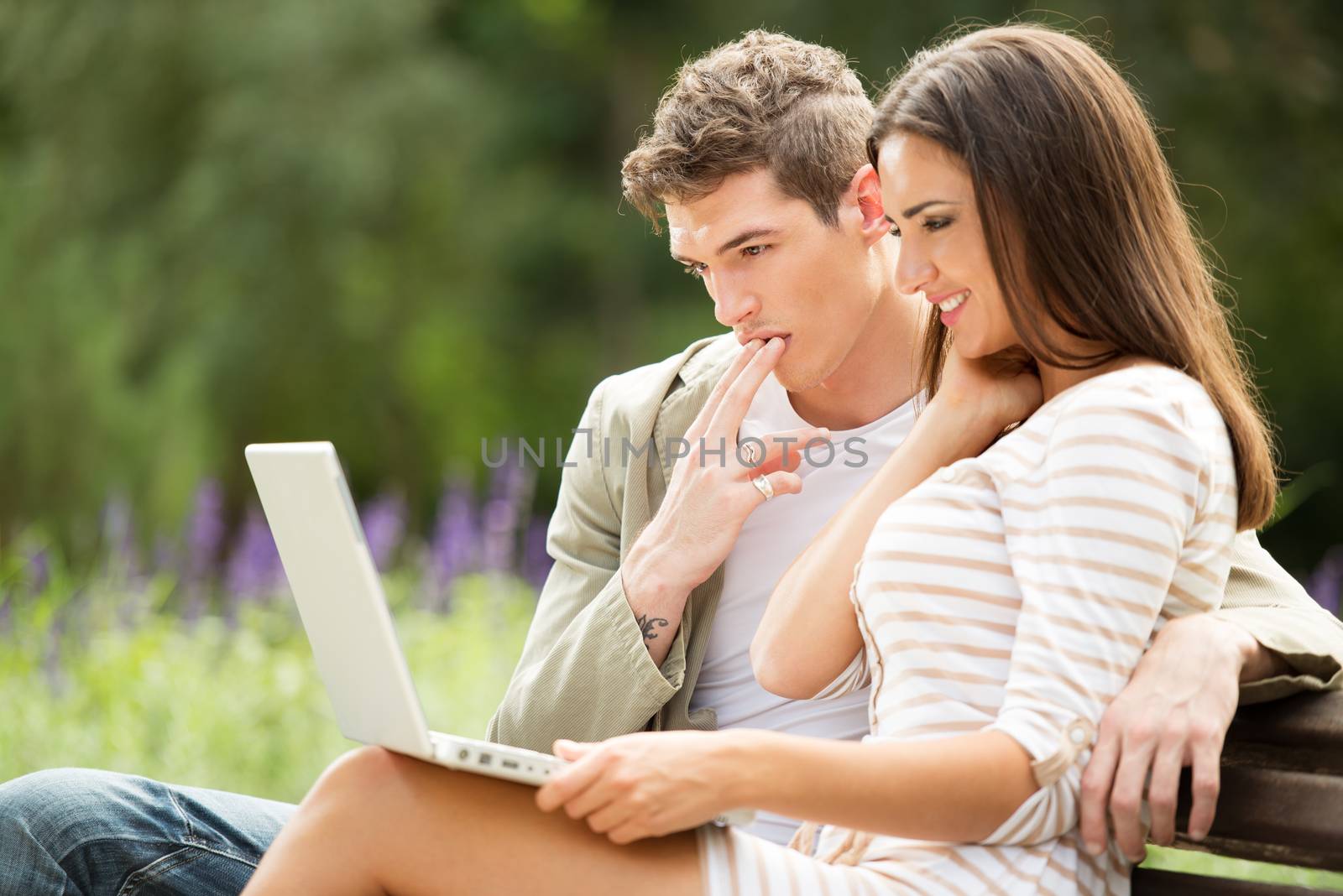 Young couple sitting on bench and using laptop at park.