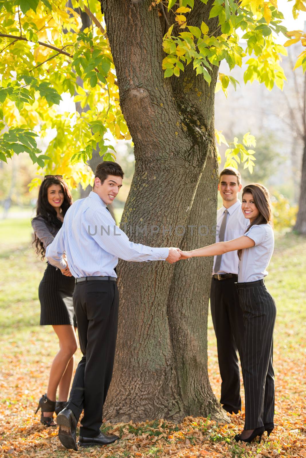 Group of young business people standing in a park hugging a tree trunk.